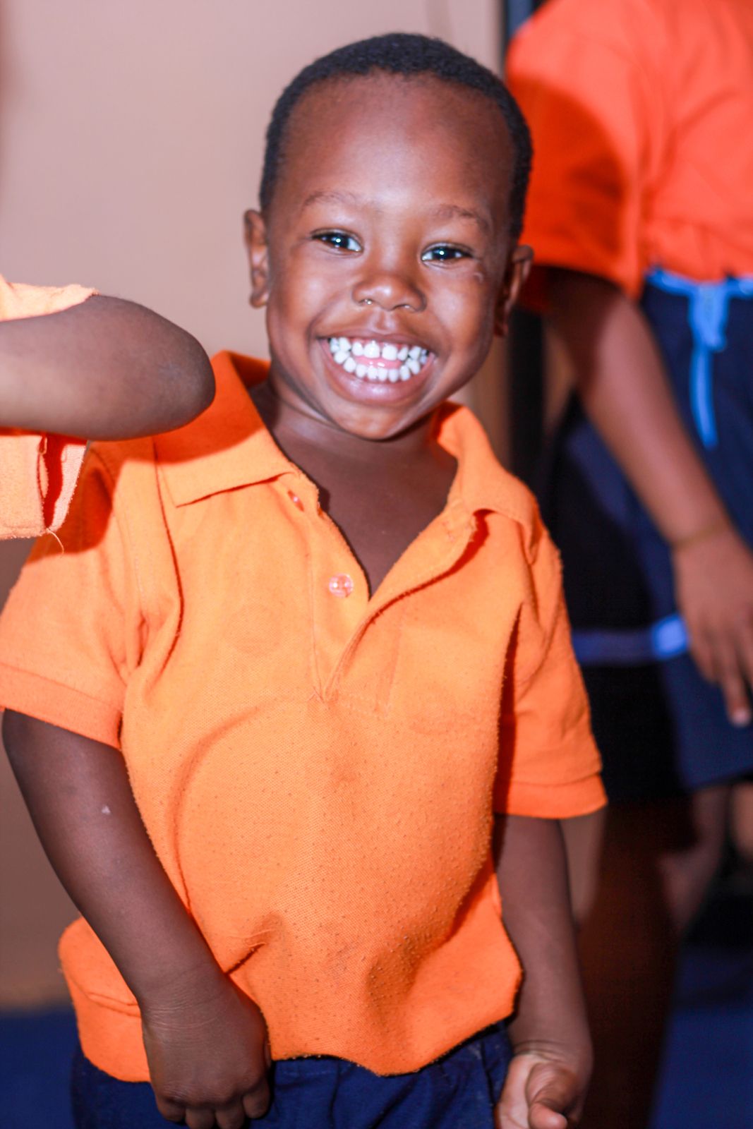 A boy in an orange polo shirt grinning at the camera