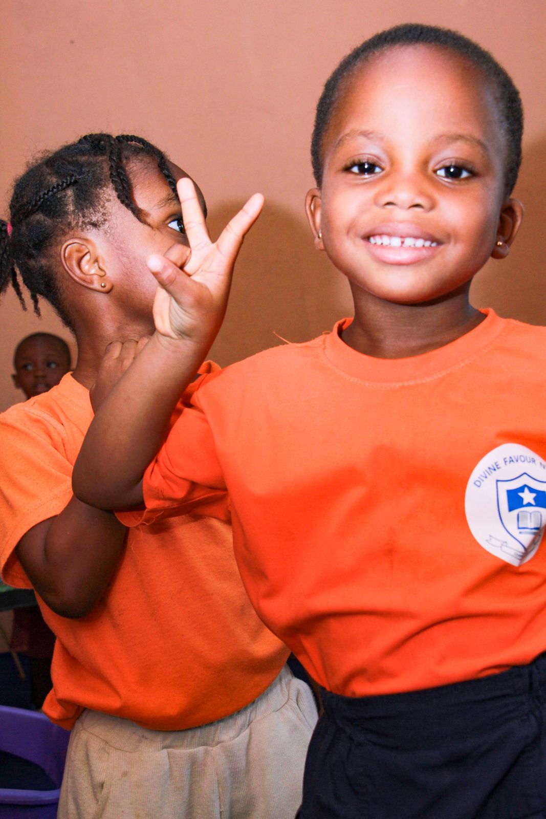 A girl in her school T-shirt smiling and making a peace sign