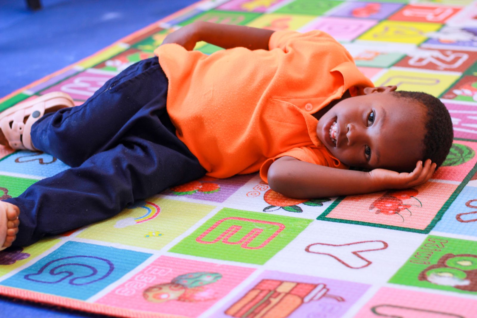 A boy resting on a colourful alphabet play mat