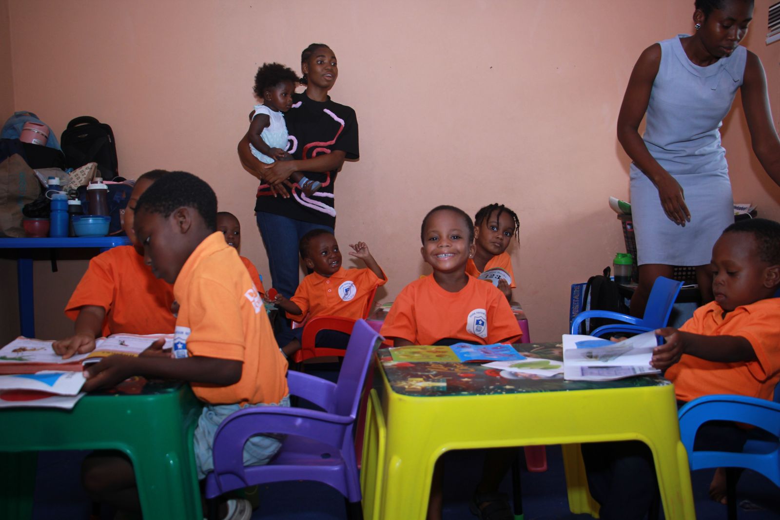Children reading at colourful tables while a teacher helps